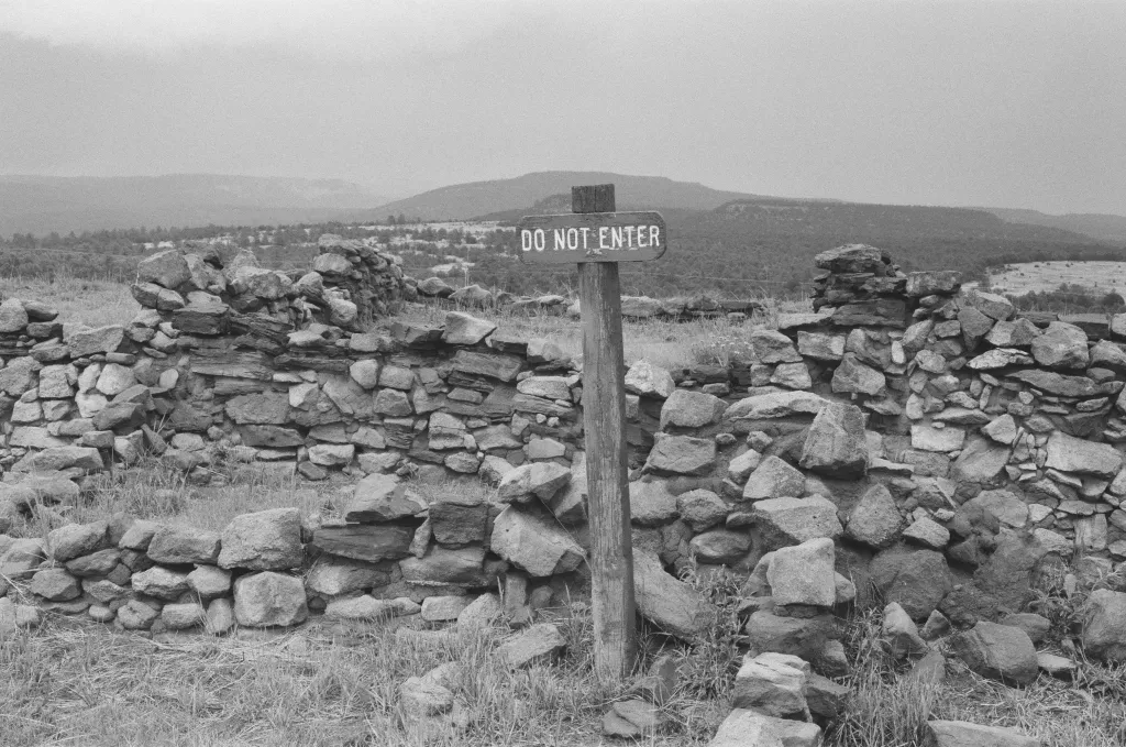Une photo noir et blanc représentant une barrière faite de pierres surplombée d'un écriteau en bois "do not enter"